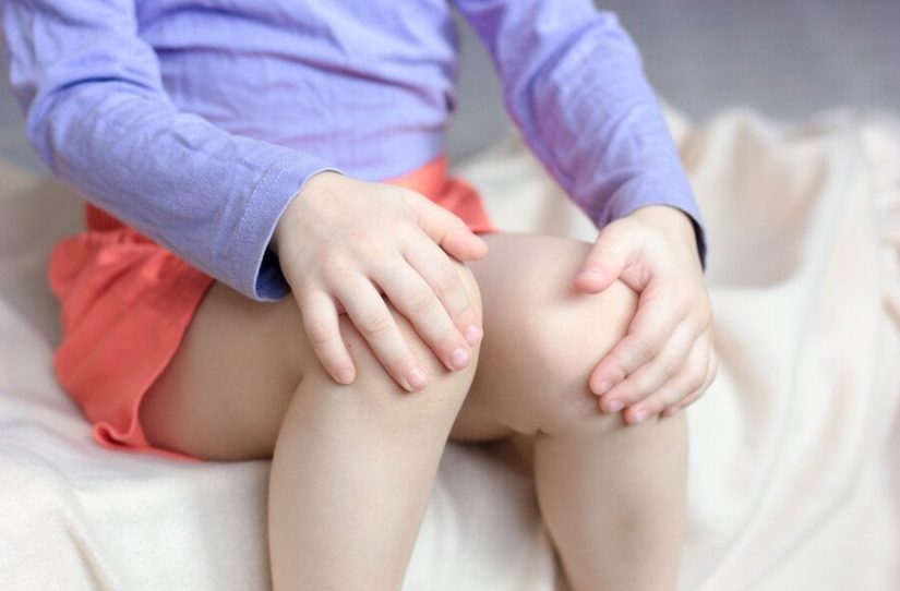 Meu filho tem dor nas pernas: criança com as mãos nas pernas